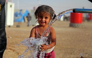 a young girl is playing with water in a refugee camp