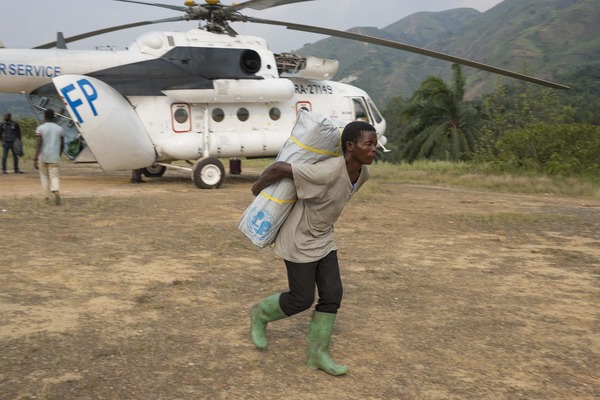 a boy carries a UNICEF pack on his back in front of an helicopter