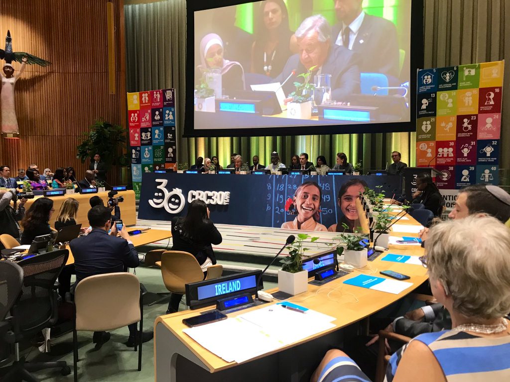 A man is speaking on a screen and is surrounded by other countries representantives