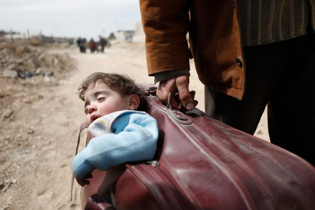 a man carrying a child in a suitcase walks towards Hamourieh where an evacuation exit from eastern Ghouta has been opened.