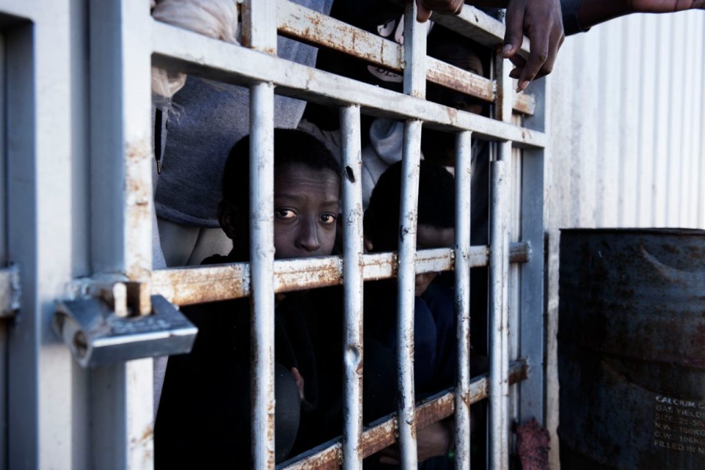 A young boy looks out from behind the bars of a cell at a migrant detention centre in Libya. 