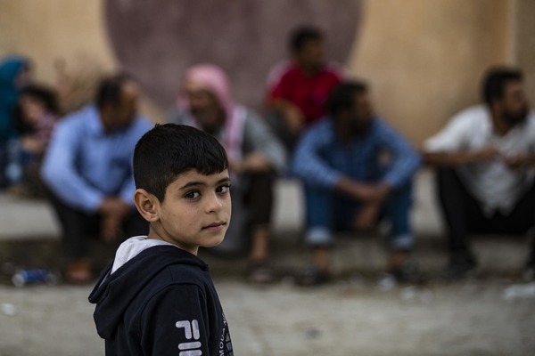 a boy stands in the street in front of men sitting 