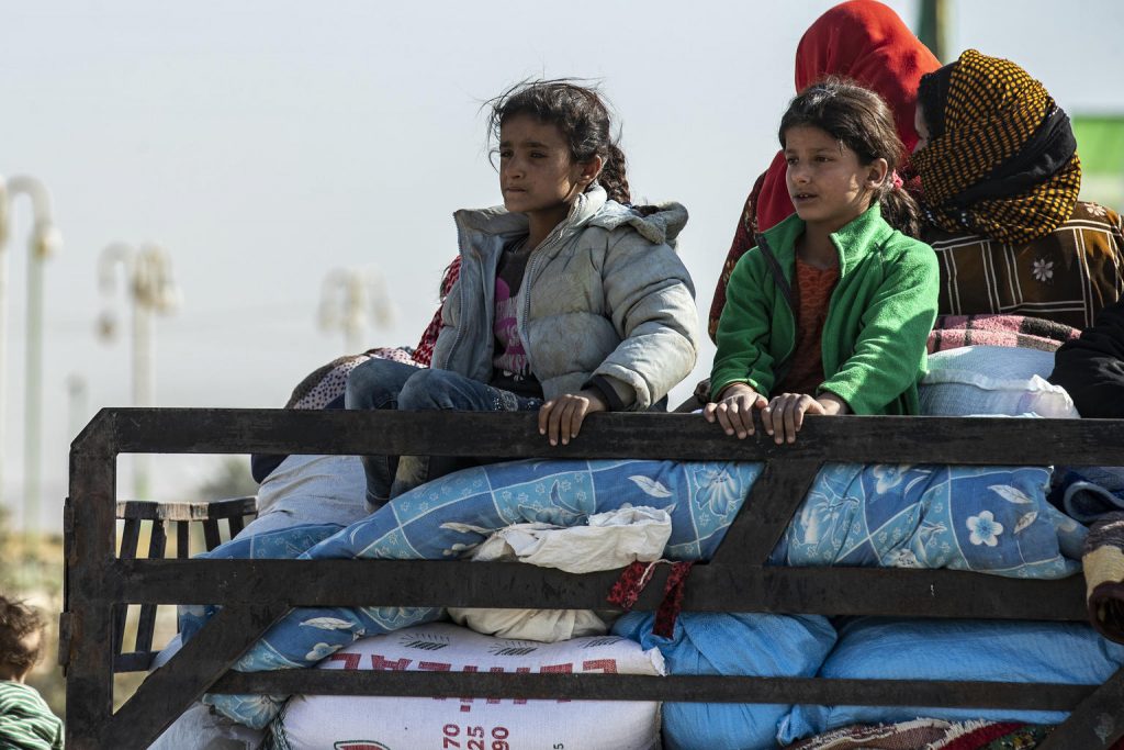 Two girls are sitting on a pile of bag behind a truck