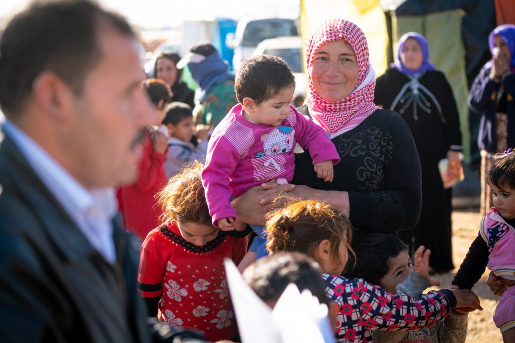 A woman carries a child while waiting in line surrounded by other children