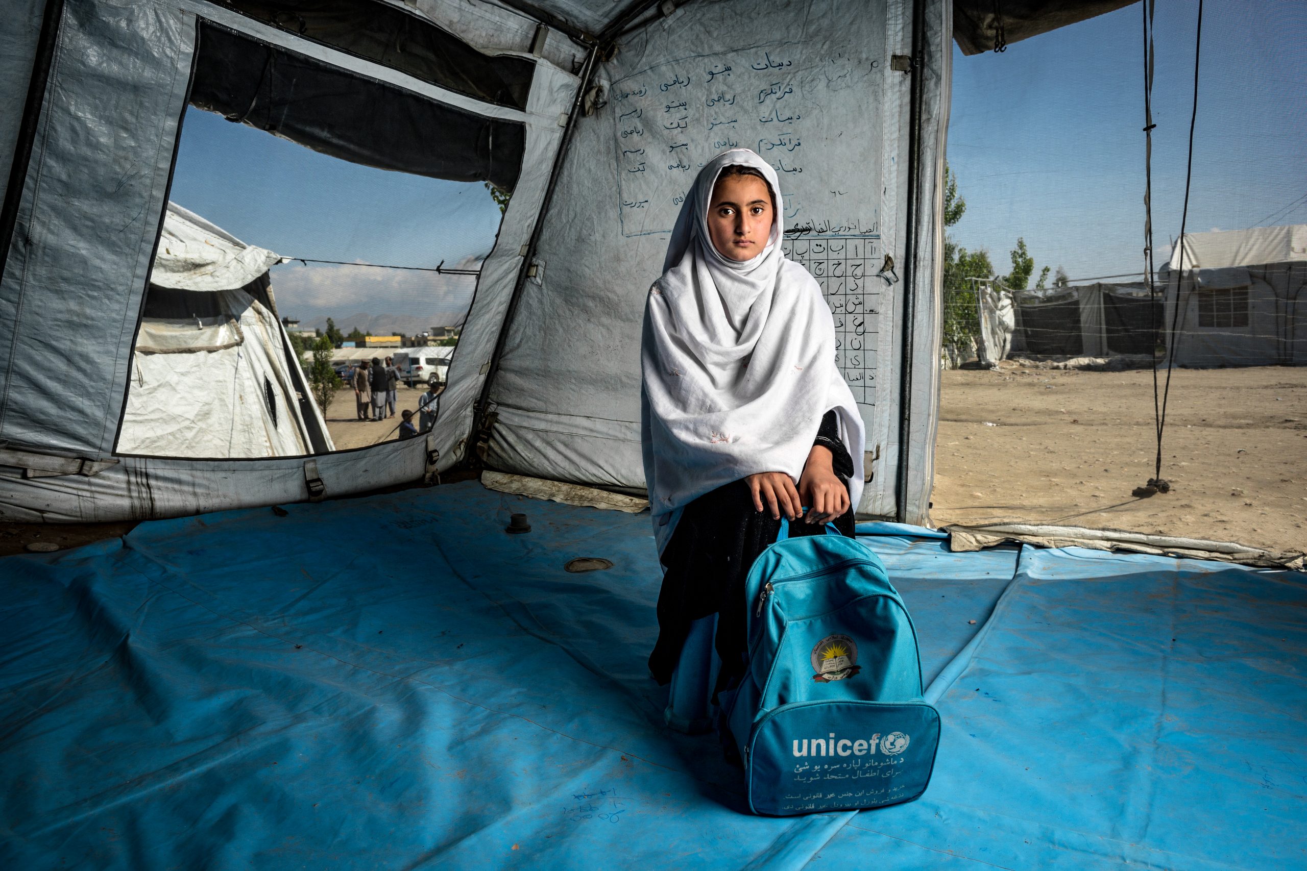 a girl is sitting in an UNICEF tent holding an UNICEF backpack