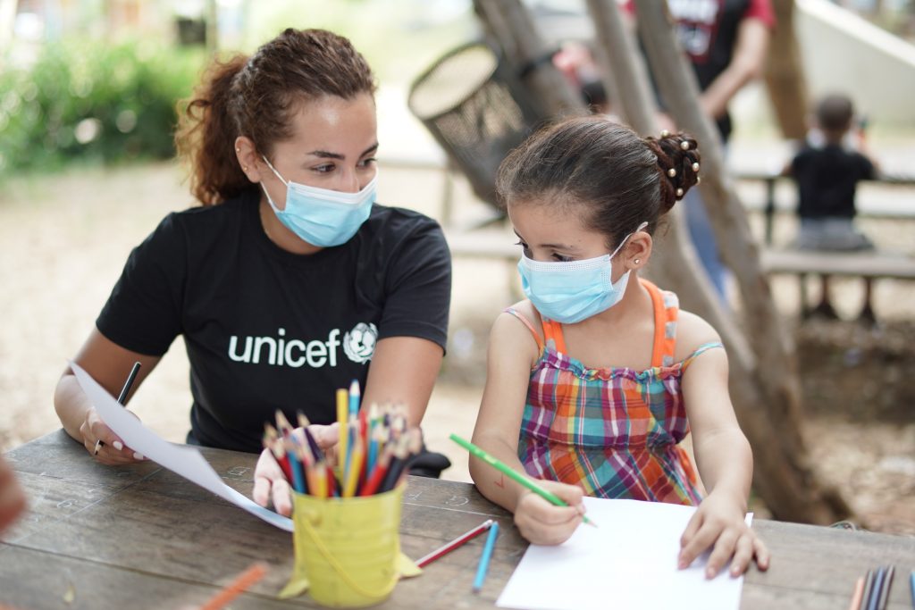 a woman is sitting at a table drawing with a little girl