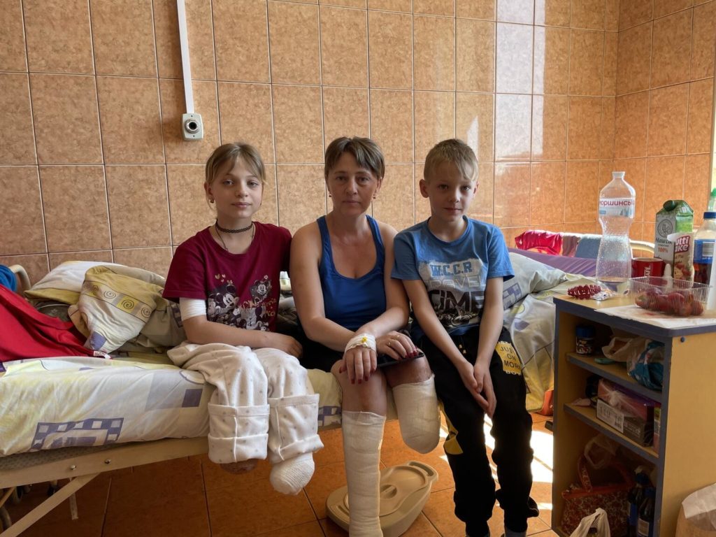 Yana, her mother and brother sit on a hospital bed