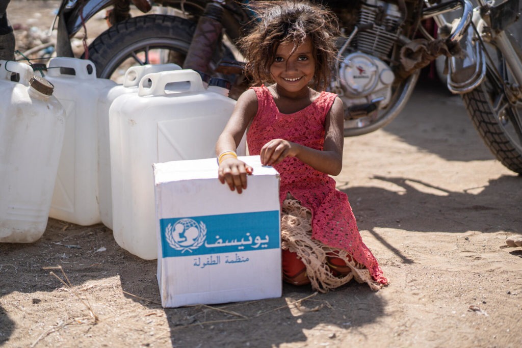 girl kneels down beside unicef box