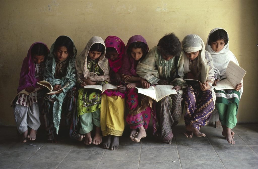 a group of girls sitting on a bench reading