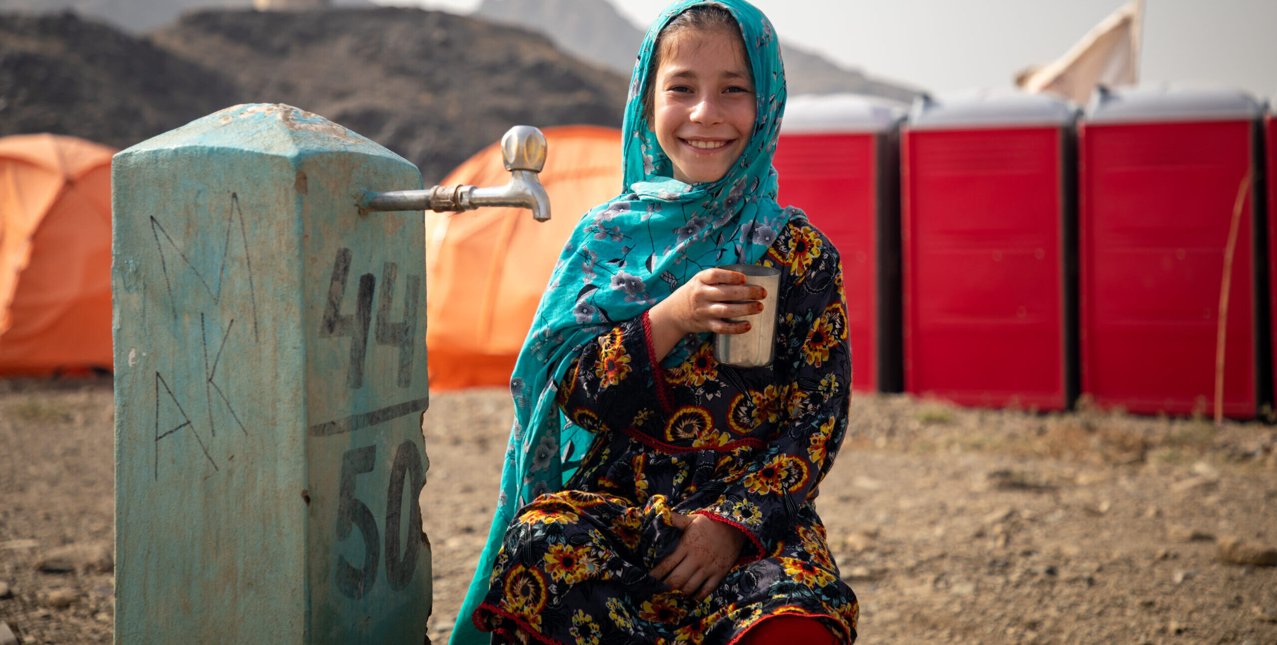 Afghani girl smiles at water pump