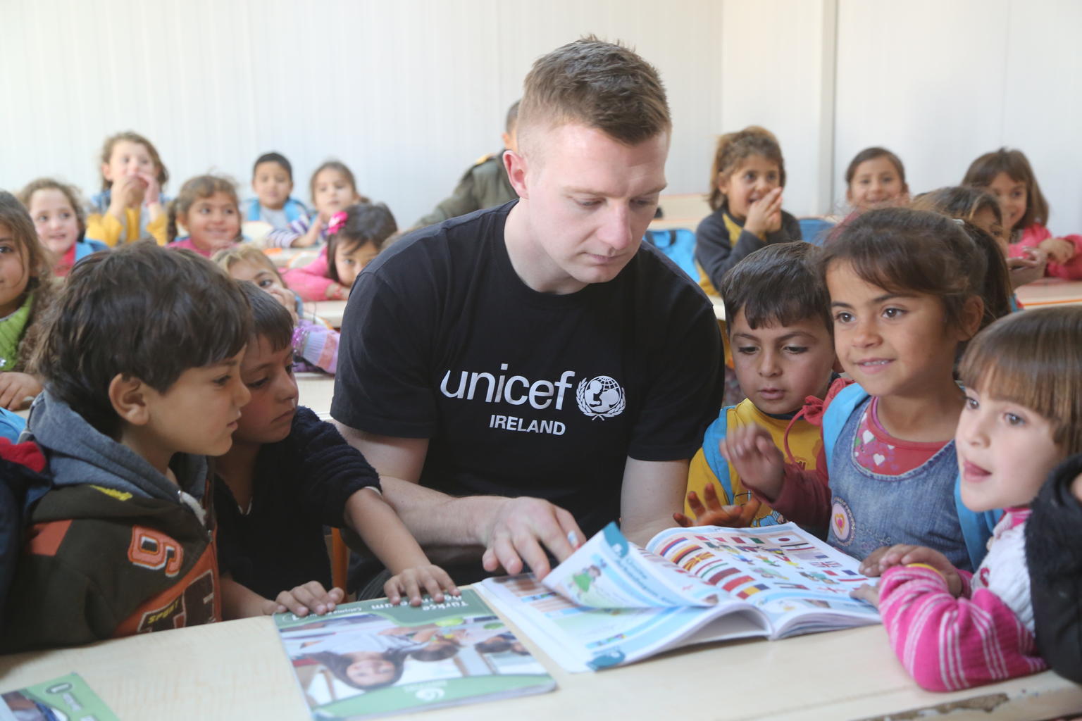 UNICEF Ambassadors like Joe Canning pictured here with children reading a book.